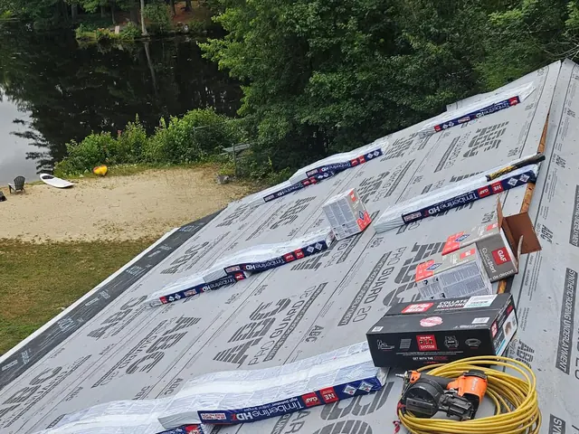 A J & J Building & Restoration roof in progress, with shingle bundles staged and a lake below